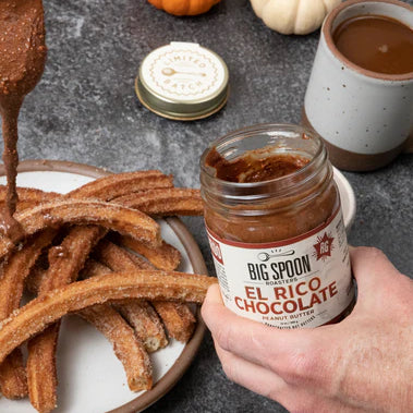 A person drizzles El Rico Chocolate Peanut Butter over a plate of churros.