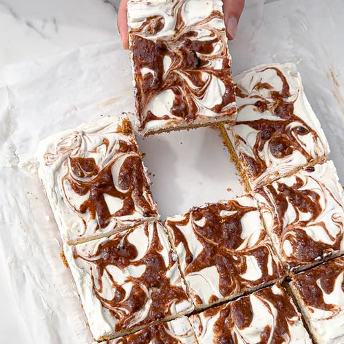 Parchment paper on a white marble background holds a no-bake cheesecake with Chocolate Sea Salt Almond Butter swirl topping.