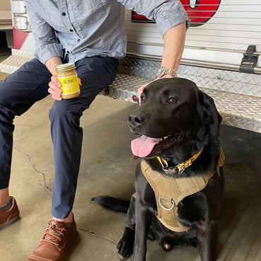 Big Spoon Roasters Co-Founder & President Mark Overbay feeds Cosmo Banana Flax Wag Butter – Peanut Butter for dogs. Mark sits on the back of the Station 13 firetruck at the Durham Fire Department.