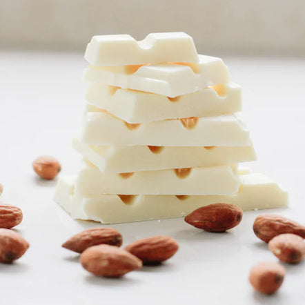 A stack of white chocolate stands vertically in front of a white background with almonds spread around it.