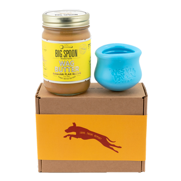 Jar of Banana Flax Wag Butter and a blue West Paw Toppl toy sit on top of a gift box with a gold and maroon decorative dog label.