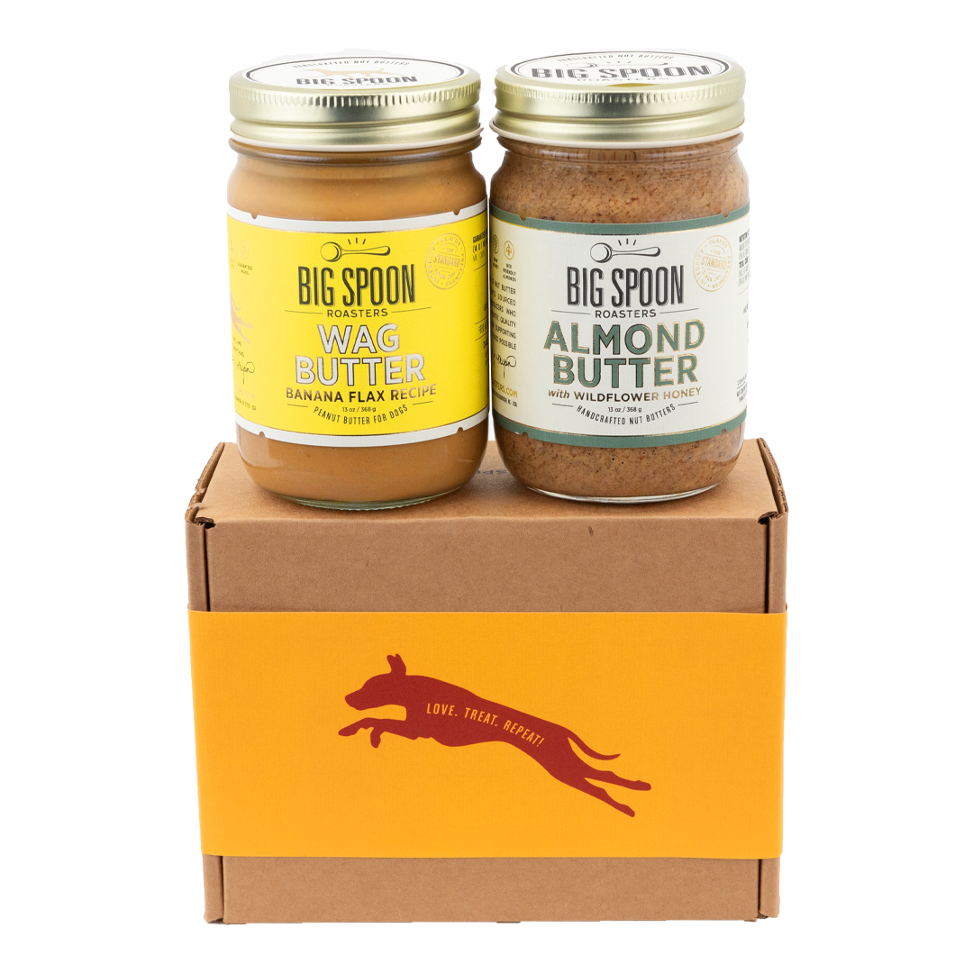 A jar of Banana Flax Wag Butter sits next to a jar of Almond Butter on top of a gift box