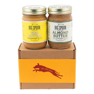 A jar of Banana Flax Wag Butter sits next to a jar of Almond Butter on top of a gift box