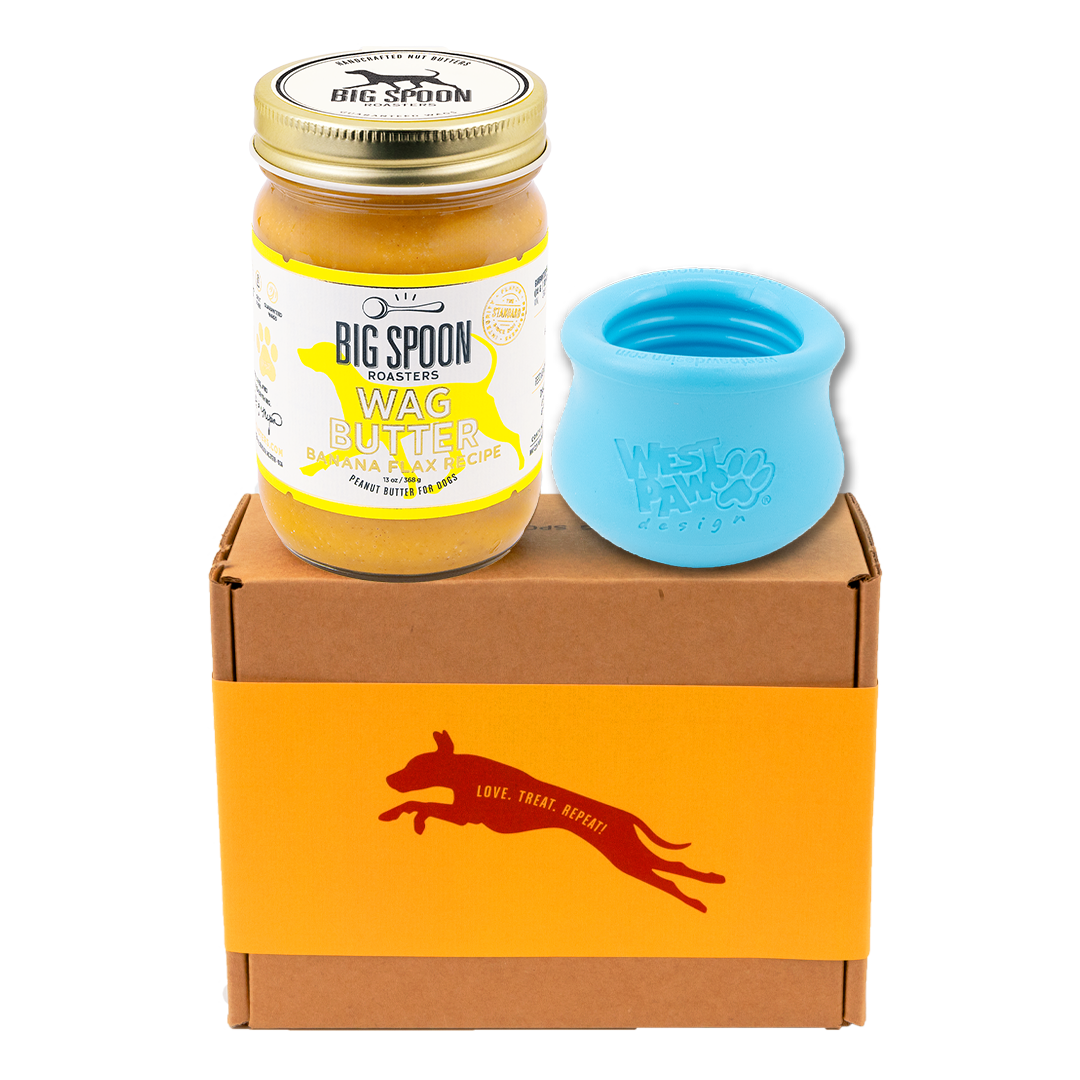 Jar of Banana Flax Wag Butter and a blue West Paw Toppl toy on top of a gift box
