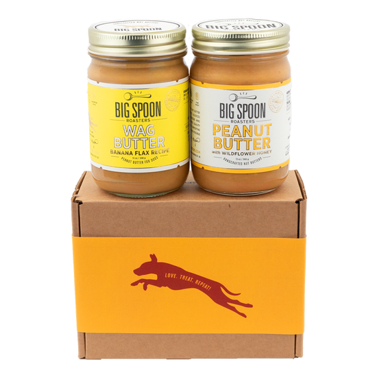 A jar of Banana Flax Wag Butter sits next to a jar of Peanut Butter on top of a gift box