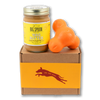 Jar of Banana Flax Wag Butter and an orange West Paw Tux toy sit on top of a gift box with a gold and maroon decorative dog label.