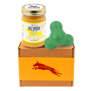 Jar of 'Big Spoon Roasters' Wag Butter on a box with a green West Paw Tux toy.