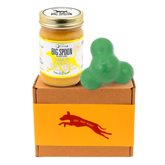 Jar of 'Big Spoon Roasters' Wag Butter on a box with a green West Paw Tux toy.
